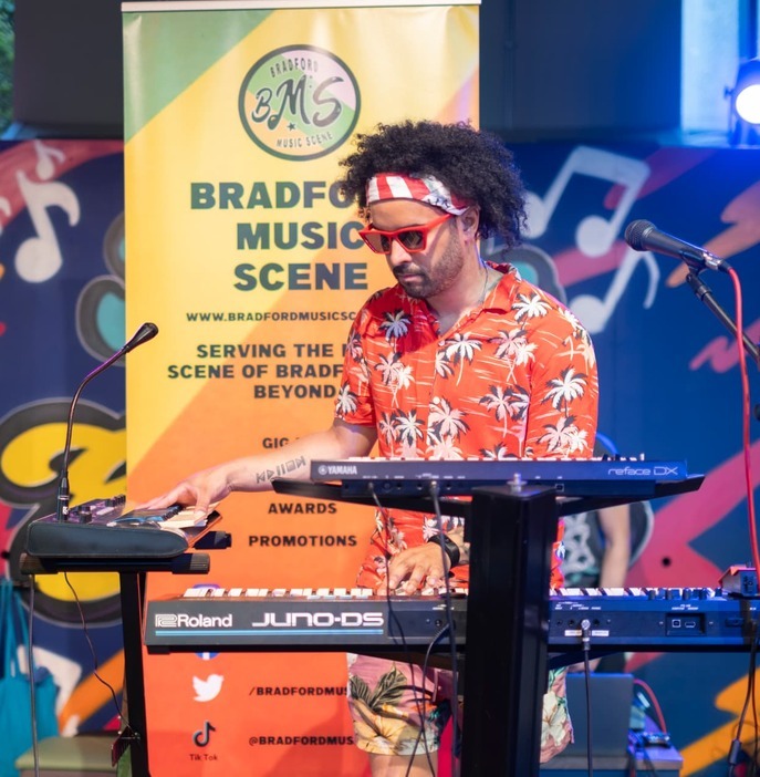 Artist performing with keyboards in front of Bradford Music Scene branding